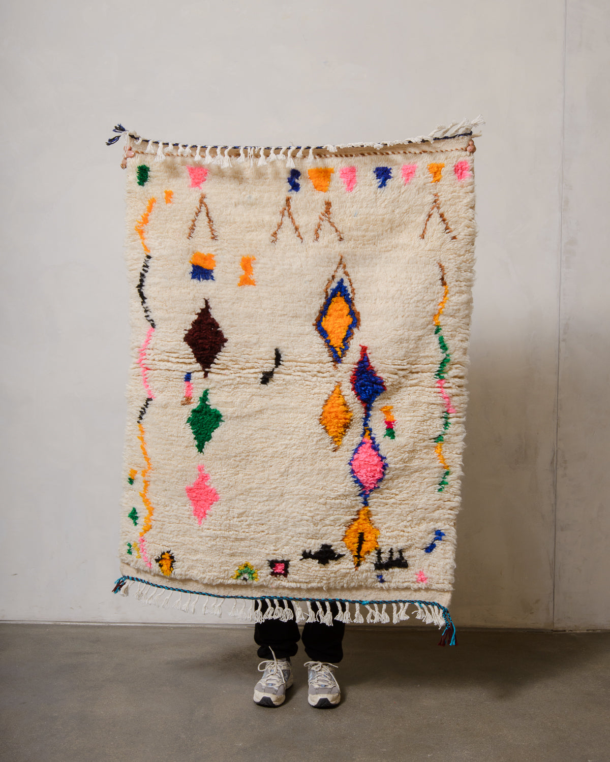 Berberlin Azilal rug in cream wool with colourful cotton being held up in front of a white wall.